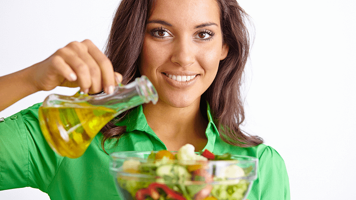 Žena pridáva olej do zeleninového šalátu